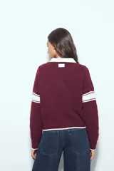 Campera de punto tipo cardigan en color bordó, con cierre frontal, cuello redondo y diseño estilo universitario. Presenta el número 54 bordado en blanco en el pecho y franjas blancas en las mangas.