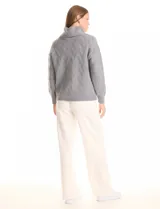 Buzo de punto grueso con textura en relieve, de cuello volcado y mangas largas con hombros caídos. Presenta puños y ruedo con terminación en rib.