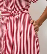 Vestido largo estilo chemise con estampado de rayas rojas y blancas, cuello clásico, cierre frontal con botones y mangas cortas amplias. Incluye un cinto desmontable para ajustar en la cintura.