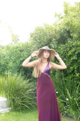 Vestido largo con estampado tie-dye en tonos violeta y fucsia, escote en V con detalles bordados dorados, cut-outs laterales bajo el busto y tirantes finos que se cruzan y atan en la espalda.