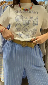 Pantalón de lino marrón con rayas verticales blancas, corte recto, cintura con elástico ancho y cinturón de rafia extraíble.