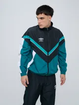 Campera deportiva Umbro modelo Beat, confeccionada en nylon ligero con diseño de bloques de color en blanco, azul marino y verde azulado. Presenta cierre frontal, cuello alto y elásticos en puños y cintura.