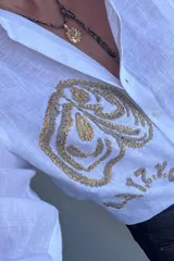 Camisa de lino color tostado, de manga larga y corte oversize, con bordado artesanal en hilo blanco en el frente y botones frontales.