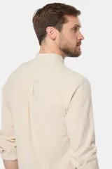 Camisa de lino color beige con cuello mao, manga larga, cierre frontal de botones y bordado sutil en el pecho.