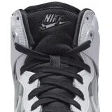 Championes Nike Dunk High con diseño de caña alta, cuerpo en cuero blanco con paneles laterales en negro brillante y detalles metálicos cromados. Presenta suela translúcida y cordones negros.