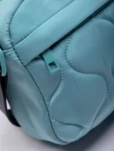 Bandolera rectangular color celeste, confeccionada en nylon reciclado con capitoneado ondulado. Cuenta con un bolsillo externo, uno interno y una correa regulable negra.