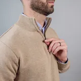 Buzo de punto color beige con cuello alto y medio cierre frontal.