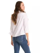 Camisa blanca de corte recto y estilo clásico, con cuello solapa, cierre frontal oculto y mangas largas con puños. Presenta dos bolsillos frontales decorados con apliques de tachas metálicas en el borde superior.