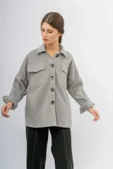 Sobrecamisa de paño color gris, con cuello camisero, cierre frontal de botones oscuros y dos bolsillos frontales con solapa. Presenta mangas largas con puños ajustables y un corte holgado.