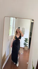 Vestido largo negro con brillos, corte irregular con abertura en la pierna, breteles finos y escote con abertura circular.