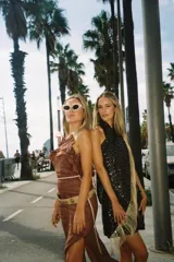 Vestido corto negro con lentejuelas, escote halter y detalle de flecos dorados en el lateral.