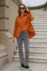 Camisa color naranja de corte amplio, con cuello camisero, cierre frontal con botones, mangas largas con puños abotonados y dos bolsillos con solapa en el pecho.