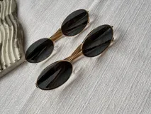 Lentes de sol estilo retro con armazón metálico dorado y formato ovalado. Cuentan con cristales oscuros y protección UV400.