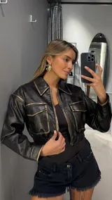 Campera corta de cuero sintético en color negro con efecto desgastado en tonos dorados en costuras y bordes. Presenta cuello camisero, cierre frontal con cremallera, dos bolsillos frontales con solapa y cintura elástica.