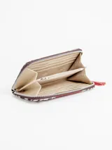 Billetera rectangular de cuero con cierre perimetral, diseño combinando laterales de pelo con estampado animal print tipo cebra y franja central roja con tachas metálicas dispuestas en forma circular. Cuenta con tirador de cierre en flecos de cuero rojo.