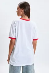 Remera blanca de corte oversize con cuello y bordes de mangas en color rojo. Presenta un estampado frontal con los personajes de Mickey y Minnie Mouse junto a la frase Cool & Chic.