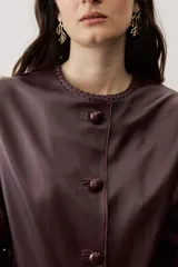 Chaqueta de cuero negra con cuello redondo, cierre frontal de botones forrados y bolsillos ribeteados con detalles de costura decorativa.