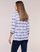Remera confeccionada en algodón liviano de silueta semi entallada, con escote en V y mangas tres cuartos. Presenta un diseño estampado que combina franjas florales en tonos violeta y rayas chevron, con un nudo decorativo en el ruedo frontal.