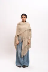 Poncho triangular tejido artesanalmente en telar manual, de lana merino color beige, con cuello alto y flecos largos en los bordes.