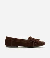 Mocasines de mujer Satinato confeccionados en cuero de gamuza marrón, con flecos, moño decorativo y costuras visibles en la capellada. Presentan punta redondeada y suela baja.