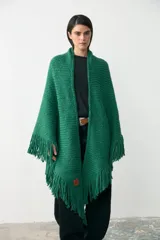 Ruana tejida en lana merino extrafina con detalles de lino y viscosa, color verde. Presenta un diseño de tejido artesanal con flecos en los bordes, ideal para usar de forma envolvente.