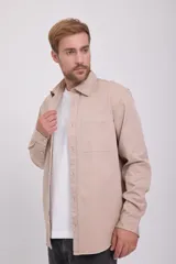 Camisa de manga larga color beige, con cuello clásico, cierre con botones y bolsillo en el pecho. Corte recto.