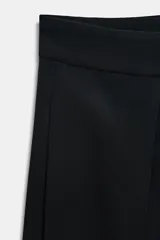 Bermudas de tiro alto color negro, con detalle de pliegues marcados en el delantero y cierre frontal con cremallera y ganchos metálicos.