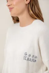 Sweater de punto color gris con bordado en color verde neón en el pecho con la frase 'GOOD KARMA'. Presenta cuello redondo, mangas largas y un diseño con tajos laterales en el ruedo.