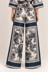 Palazzo amplio de seda con estampado paisajístico y bordes en tono azul marino. Cuenta con cintura elástica con cordón ajustable y bolsillos laterales.