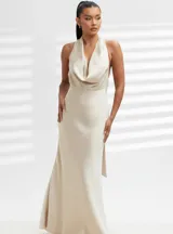 Vestido largo de satén color beige, con escote halter y espalda descubierta. Presenta un diseño minimalista con corte fluido y acabado brillante.