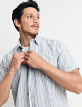 Camisa de manga corta a rayas verticales en tonos celeste, verde y blanco, con cuello clásico y bolsillo en el pecho. Cierre frontal con botones. Corte recto.