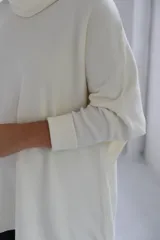 Polerón de punto color crudo, con cuello alto tipo polera, corte holgado y mangas largas con puños acanalados.
