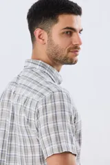 Camisa de manga corta confeccionada en mezcla de lino y algodón, con diseño a cuadros en tonos gris, blanco y azul. Presenta cuello camisero con botones y bolsillo ojal en el pecho con detalle bordado.
