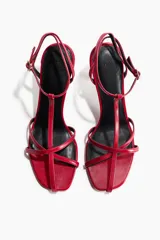 Sandalias rojas de taco fino y alto, con diseño de tiras finas en el empeine, tira en T y pulsera ajustable con hebilla en el tobillo.