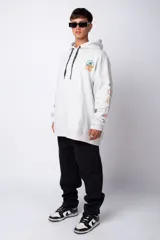 Buzo canguro gris claro de corte oversize, con capucha y cordones negros con letras blancas. Presenta un bolsillo tipo canguro y un estampado pequeño en el pecho y otro en la manga.