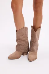 Bota de caña media en gamuza color beige, con diseño slouchy y detalle de strass aplicado en toda la caña. Presenta taco cuadrado y punta almendrada.