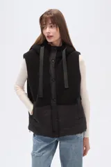 Chaleco con capucha, diseño bicolor que combina textura de corderito en la parte superior y material técnico liso en la parte inferior. Cuenta con cierre frontal y botones a presión.