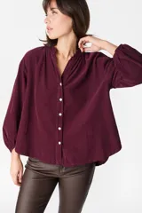 Camisa de pana color bordó, con cuello mao, cierre frontal de botones y mangas largas abullonadas con puños elásticos.