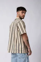 Camisa de manga corta con cuello clásico y cierre frontal de botones. Confeccionada en tejido de punto crochet calado, presenta un patrón de rayas verticales negras sobre fondo crudo.