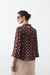 Camisa de manga larga color marrón con estampado de lunares blancos, cuello mao y cierre frontal con botones.