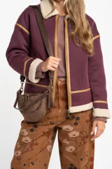 Campera tipo gamulán de color bordó, con interior y cuello de corderito sintético en tono crema. Presenta detalles de ribetes en cuero sintético color suela, cierre frontal metálico y bolsillos laterales.