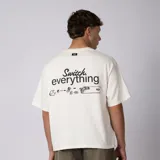 Remera boxy de color crudo con hombro caído y corte cuadrado a la cadera. En el frente presenta un diseño minimalista con texto y un pequeño logo central.