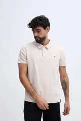 Remera polo de manga corta con textura sutil y corte clásico, confeccionada en algodón color beige. Cuenta con cuello camisero y cartera con dos botones en el frente, además de un pequeño bordado en el pecho.