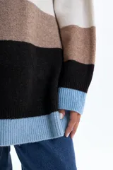 Buzo de tejido de punto con diseño de franjas horizontales en bloques de color verde, blanco, marrón, negro y celeste. Presenta cuello redondo, mangas largas y un corte holgado.