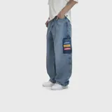 Pantalón de jean corte ultra baggy, color azul lavado, con bolsillo lateral tipo cargo que presenta tres parches rectangulares bordados en colores azul, amarillo y rojo con la inscripción Venefoclub.
