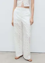 Pantalon de tiro medio con diseño recto y largo, confeccionado en tejido de algodón con bordado floral y detalles calados. Cuenta con cierre delantero de botón, gancho y cremallera ocultos, trabillas y bolsillos laterales.