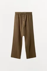 Pantalón tipo baggy de tiro bajo, confeccionado en mezcla de lino. Presenta cintura elástica con cordón ajustable, cierre frontal con botones y falsos bolsillos de vivo en los laterales.