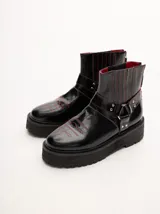 Bota corta de cuero negro tipo biker, con suela track de goma, plataforma, costuras y bordados decorativos en hilo rojo. Presenta tiras con hebillas metálicas y cierre en la parte trasera.
