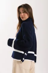 Sweater azul marino de punto con cuello alto, mangas largas con puños blancos y detalle de botones en el lateral.
