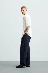 Sobrecamisa negra de tejido con elasticidad, cuello solapa y manga corta. Tiene dos bolsillos de plastrón en el pecho y cierre frontal con botones a presión.